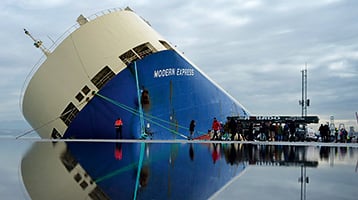 Modern Express listing in the Port of Bilbao, viewed across a water puddle on the quay.